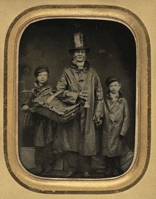 Lot 116 - Ambrotype of a street vendor holding his basket and a bell with his two young assistants, c. 1860